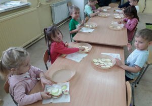 Dzieci przy stoliku wykonują susz jabłkowy, układają plastry jabłek na pergaminie.