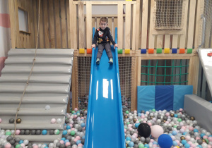 Sala zabaw. Chłopiec zjeżdża na zjeżdżalni.