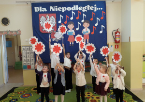 Dzieci radośnie wiwatują biało- czerwonymi kwiatami.