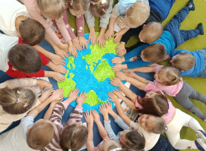 Dzieci leżą na dywanie i dotykają rękami plakatu z kulą ziemską