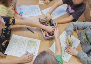 Dzieci siedzą przy stoliku i kolorują wydrukowane scenki