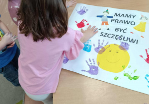 Dziecko odciska rękę umoczoną w farbie na plakacie