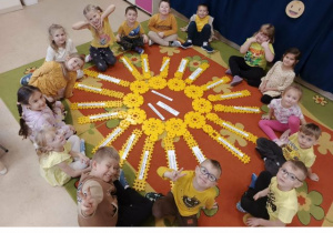 Przedszkolaki siedzą w kole, w środku leży słońce ułożone z żółtych klocków.