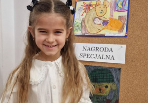 Dziewczynka pozuje do zdjęcia, w tle praca konkursowa.