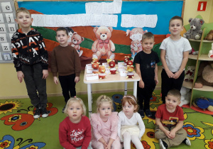 Dzieci na tle dekoracji Święto Pluszowego Misia prezentują misia wykonanego z jabłek.