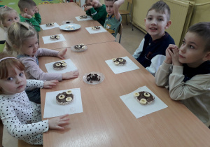 Dzieci przy stolikach prezentują wykonane misiowe przysmaki.