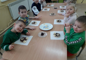 Dzieci przy stolikach prezentują wykonane misiowe przysmaki.