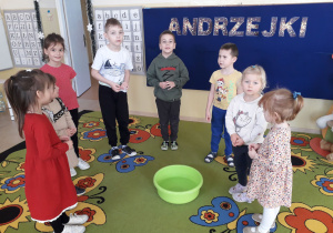 Dzieci wrzucają grosze do miski z wodą by zacząć andrzejki.