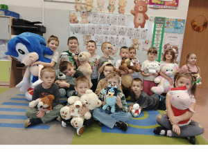 Dzieci siedzą i trzymają przed sobą misie. W tle dekoracja.