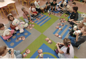 Dzieci siedzą w kole i trzymają swoje misie. Przed nimi misiowe obrazki ułożone z części.