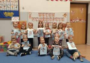 Dzieci w grupie trzymają swoje prace plastyczne z misiem.