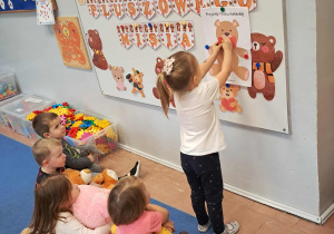 Dziecko przyczepia na tablicę misia.