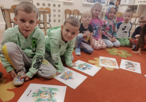 Dzieci siedzą na dywanie, przed nimi leżą obrazki ze znanymi misiami z bajek.