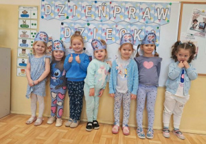 Dzieci ubrane na niebiesko pozują do zdjęcia, w tle tematyczny napis.