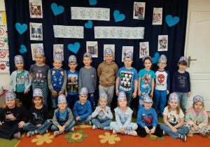 Grupa starsza pozuje do zdjęcia, na głowach mają niebieskie opaski. W tle dekoracja z obrazkami tematycznymi i nibieskimi sercami.