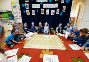 Dzieci siedzą w kole, w środku leżą obrazki tematyczne.