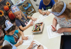 Przedszkolaki siedzą przy stoliku i kolorują obrazki.