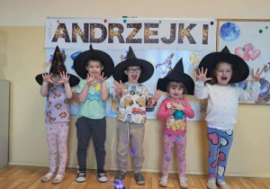 Dzieci w czarnych kapeluszach pozują do zdjęcia, w tle napis andrzejki.