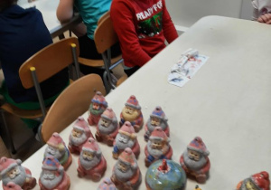 Chłopiec siedzi przy stoliku i podziwia pomalowane skarbonki.