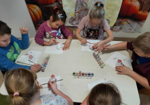 Dzieci siedzą przy stoliku i malują ceramiczne skarbonki w kształcie Mikołaja.