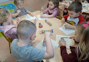 Dzieci siedzą przy stoliku i malują ceramiczne skarbonki Mikołaje