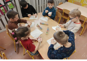 Dzieci siedzą przy stoliku i malują ceramiczne skarbonki Mikołaje