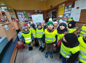 W urzędzie pocztowym. Dzieci pozują do fotografii, chłopiec trzyma w rękach kopertę z listami do Mikołaja