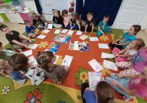 Dzieci z grupy 5, 6 latków siedzą na dywanie w kole prezentując swoje rysunkowe listy do mikołaja.