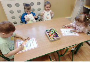 Kolejna grupa 3, 4 latków siedzi przy stoliku w sali przedszkolnej, rysują kredkami na kartce wymarzone prezenty.