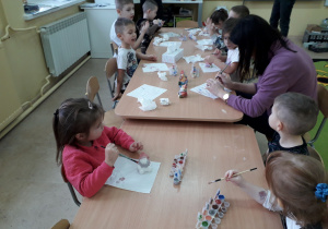 Dzieci przy stolikach malują figurkę Mikołaja.