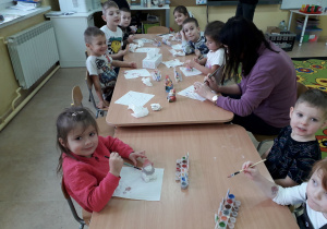 Dzieci przy stolikach malują figurkę Mikołaja.