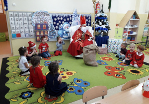 Dzieci siedzą na dywanie i słuchają opowiadania Św. Mikołaj, który siedzi w mikołajowym fotelu.