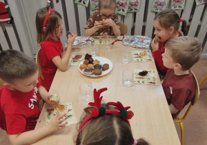 Dzieci siedzą przy stolikach i jedzą babeczki.