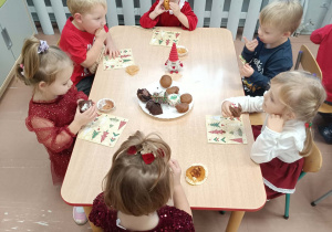 Dzieci siedzą przy stolikach i jedzą babeczki.