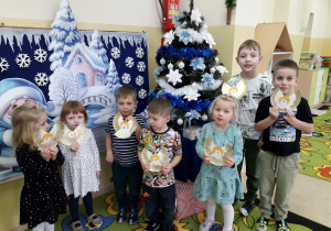 Dzieci na tle choinki prezentują wykonaną dekorację - aniołek na choinkę.