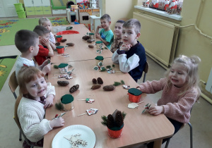 Dzieci przy stolikach komponują świąteczny stroik.