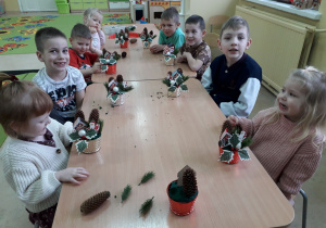 Dzieci przy stolikach prezentują wykonane stroiki.