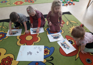 Dzieci na dywanie konstruują żłobek z wyciętych postaci.