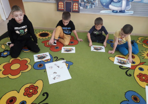 Chłopcy na dywanie konstruują żłobek z wyciętych postaci.