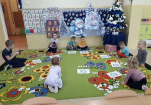 Dzieci na dywanie uczą się odejmować z wykorzystaniem sylwet postaci ze żłobka.