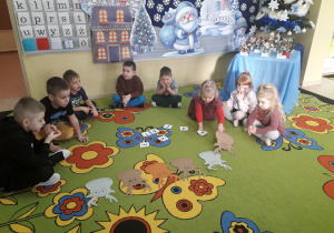Dzieci na dywanie przyporządkowują cyfrę do danego renifera.