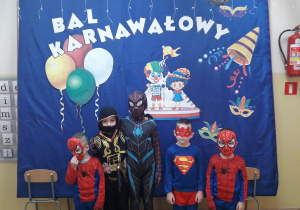 Chłopcy w strojach superbohaterów pozują do zdjęcia. W tle karnawałowa dekoracja.