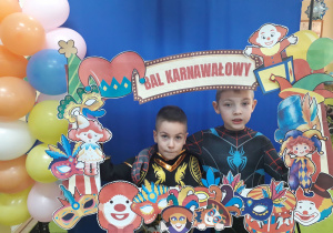 Dwoje chłopców strojach superbohaterów pozuje w fotobudce.