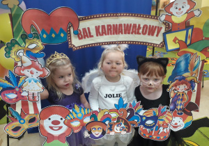 Dziewczynki w strojach aniołka, kotki i księżniczki pozują w fotobudce.