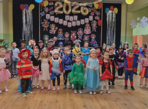 Dzieci stoją w przebraniach. W tle dekoracja.