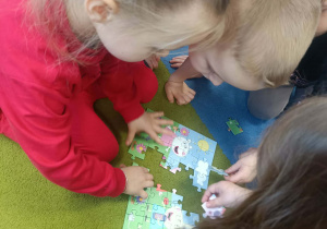Dzieci układają na dywanie puzzle.