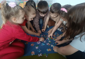 Dzieci z grupy młodszej układają na dywanie puzzle.