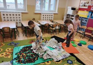 Dzieci spacerują po ścieżce sensorycznej wykonanej z kamieni sensorycznych, kasztanów, klocków, gazet i folii bąbelkowej.