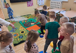 Przedszkolaki spacerują po ścieżce sensorycznej wykonanej z kamieni sensorycznych, kasztanów, klocków i folii bąbelkowej.