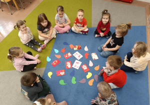 Dzieci w kręgu siedzą na dywanie. W środku połówki serc